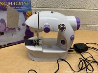 Mini white and purple sewing machine with power adapter and connected cords.