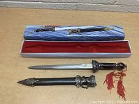 Mini sword/dagger with sheath and decorative box, laid out on a table, showing detailed hilt and scabbard decorations and the box design.