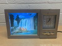 View of the vintage clock with illuminated waterfall scene and analog clock face showing approximate time 12:04.