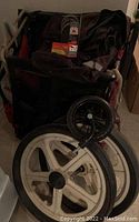 Photo of the bike chariot trailer folded with two large white wheels and two smaller black wheels stacked in front. Accessories like the bike bag and LED taillight visible on top.