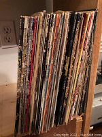 Photo of side view of approximately 40 LP records stored upright showing varied album cover spines with worn edges.