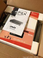 Box and user manual of the Apex DVD player inside the packaging showing the player is new in box.