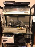 Top three shelves on metal and glass rack showing two Panasonic disc players, white belt-drive turntable and bag of cables