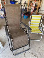 Photo showing brown gravity chair with woven fabric and black metal frame, positioned next to white folding lawn chair with yellow striped fabric and a carrying strap.