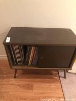 Front view of dark wood cabinet with one sliding door open revealing LPs.