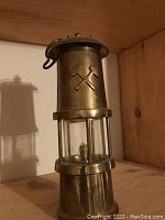 Front angle view of the vintage Century Mining Equipment Inc. miners lamp showing the glass section and hammer and pickaxe emblem.