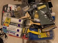 Photo showing new paint rollers, roller covers, paint brushes and a paint tray, all sealed in plastic packaging and bundled together.