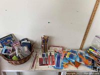 Overview image showing basket of office supplies along with pencils in glass jar, pens and markers in packaging, and loose items on table including ruler.