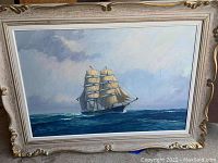Full view of the framed ship painting showing the ornate wooden frame and the ship on ocean with cloudy sky.