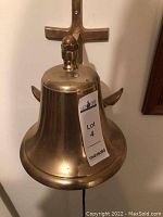 Front view of brass ship's bell with identifying lot sticker, highlighting the bell and mount shape.