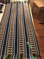 Photo showing one of the multicolor braided fabric runners with fringed ends on a wooden floor near a chair and table