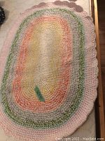 Oval knitted/crocheted pastel-colored rug with scalloped border edge
