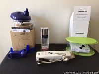 Photo of unused kitchen items: Tupperware Quick Chef chopper with box and purple lid, 2.1 inch ice cream scoop with black handle, Chefables fruit and veggie keeper with green lid, and Think Kitchen oil sprayer bottle.
