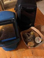 Two welding helmets and small soldering supplies in brown container