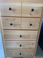 Front view of wooden dresser showing five drawers with black knobs.