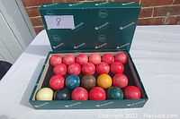 Set of 22 billiard balls arranged in original Aramith box, showing multiple colors and glossy finish.