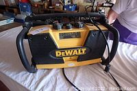 Front view of yellow and black DeWalt portable jobsite radio with control knobs and speakers, showing power cord and handle protection frame.