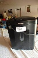 Full view of black Fellowes electric paper shredder with power cord and waste bin window visible