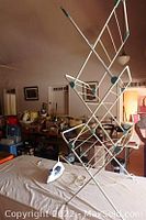 Electric iron placed on a flat surface alongside a foldable drying rack in a room with various items around.
