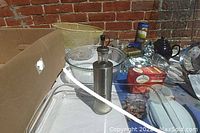 Wide shot of kitchen supplies including glass baking dishes, mixing bowls, metal oil dispenser, kitchen utensils, and spice containers on a table outside.