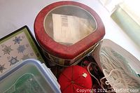 Top view showing red metal tin box, red pincushion, clear plastic lids, and fabric pieces