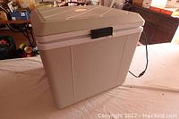 Full view of portable beige plastic cooler/heater with lid closed and power cord visible on table.