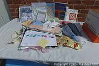 Overall lot photo showing variety of fabric pieces, pattern booklets, and instruction books spread out on a table.