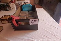 Brown rectangular box with leather trim placed on a flat surface, containing several small plastic containers and pincushions.