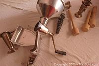 Overall view of the Squeezo strainer with main attachments including crank, funnel, clamp base, spiral auger, and wooden tools
