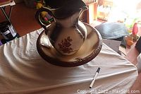 Photo showing water pitcher on top of matching bowl on table, pen for scale.