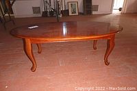 Front angled view of wooden coffee table showing oval top, polished finish, and curved legs.