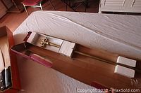 Curtain rod with attached decorative finials in cardboard packaging lying on a bed.