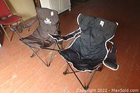 Front and side view of two outdoor folding camping chairs, one black and one dark brown, placed on a reddish floor, showing their size and condition.