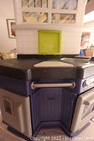 Close up photo of the corner and handle of the Little Tikes child's oven and stove play centre showing purple base, black stove top, and green compartment.