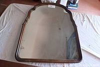 Full view of the wood framed mirror lying flat on a cloth surface showing the decorative shaped top edge of the frame and reflective surface.