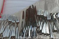 Multiple forks, knives, and spoons arranged on paper showing polished stainless steel flatware.