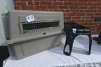 Beige kennel crate with metal front door and black elevated dog dish holder on white surface against brick background