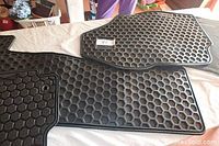 Three black rubber car floor mats shown on a table, each with a hexagonal honeycomb surface pattern for grip and dirt containment.