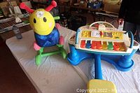 Wide shot of the colorful baby’s rocker and battery-operated zylophone toy placed on a table.