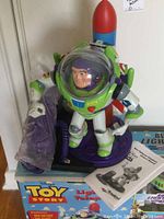 Side angled view of the Buzz Lightyear telephone toy showing figure and handset attached by cord, placed on box with manual nearby.