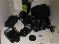 Overview of camera with attached lens, two Contax flash units, lens cap, and carrying cases on white surface.