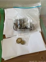 Overview of white envelopes stacked with plastic bags containing various circulated coins, some envelopes appear empty.