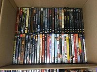 Box containing two rows of various DVDs including Harry Potter series, Gladiator, and more.