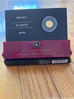 Black outer sleeve and red presentation box showing gold coin in capsule