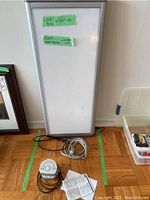 Photo showing the light box with a green tape label indicating dimensions 16.5x40x2.5 and Sony Dream Machine clock radio and extension cord on the floor in front.