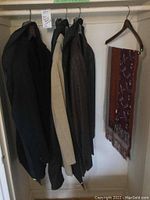 Four men's jackets hanging inside a closet: black, beige, and two darker wool blazers, plus a multicolored silk scarf hung on a wooden hanger.