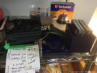 Photo showing Iomega Zip drive with multiple Zip disks on metal shelf alongside headphones, Verbatim DVD-R, and a metal-floss Mayday hanging lamp.