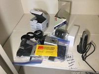 Lot contents on white surface showing Canon camera, Yashica lens box, Rodenstock magnifier box, cellphone, cables, and cleaning paper.