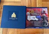 Closed blue presentation case with RCMP embossed crest and anniversary years with booklet insert showing set information and RCMP mounted police image.
