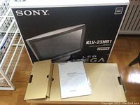 Sony KLV-23HR1 23-inch LCD TV in original box with accessory and manual boxes on floor with wooden parquet.